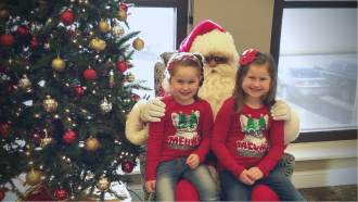 two sisters sitting on santa's lap beside a christmas tree